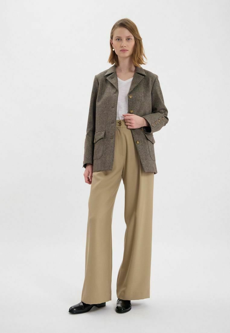 Blazer en tweed marron avec deux poches et des boutons dorés, associé à un pantalon beige taille haute et des chaussures noires. Chemise blanche en dessous.