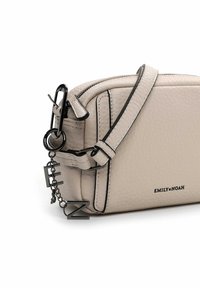 Borsa a tracolla beige con texture, dotata di zip, tracolla regolabile e accessori neri. Presenta un ciondolo con le lettere E e Z su una catena.