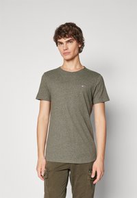 Olivgrön kortärmad t-shirt med rund hals, tillverkad av strukturerad tyg, med en liten röd och vit logo på vänster bröst.