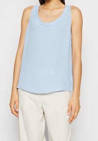 Jasnoniebieski bezrękawnik z okrągłym dekoltem, wykonany z gładkiego materiału. Design posiada luźny krój i lekko zaokrąglony dół.
