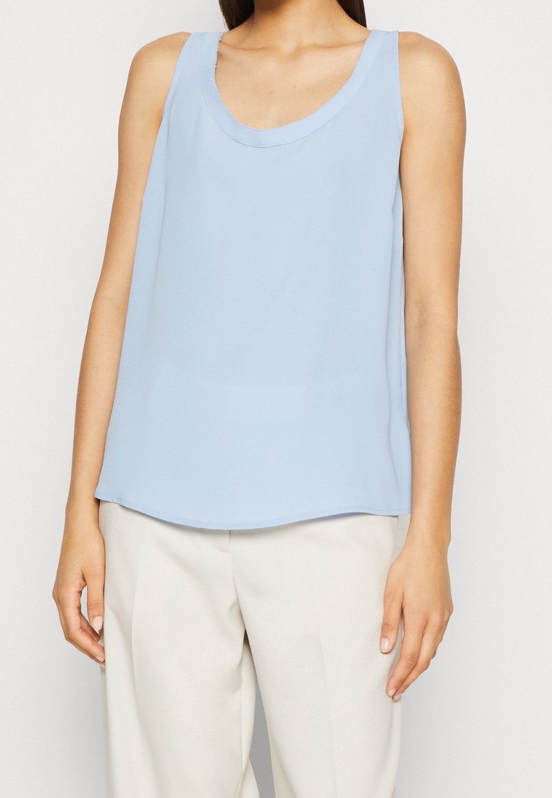 Jasnoniebieski bezrękawnik z okrągłym dekoltem, wykonany z gładkiego materiału. Design posiada luźny krój i lekko zaokrąglony dół.