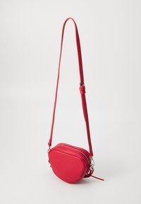 Sac en cuir rouge à bandoulière, de forme arrondie, avec fermeture éclair et bandoulière réglable. Texture lisse avec des accents matériels minimaux.