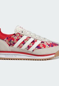 Röda och vita sportskor med blommönster, i mocka och textilmaterial, tre vita ränder, gummisula och texturerad hälkappa.