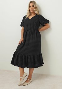 Mustapilkkuinen mekko lyhyillä hihoilla, V-pääntiellä, vyötäröltä vyötäröltä kiristetty, ja kerroksellinen liehukhemmo. Yhdistetty vaaleanbeigeihin loitouchin. Sileä rakenne.