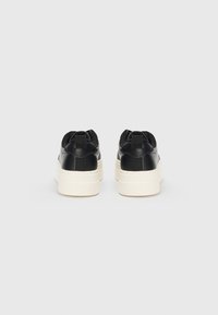 Zapatillas negras con parte superior de cuero liso, suela de goma blanca y tira en el talón. Diseño de punta redondeada con suela texturizada.