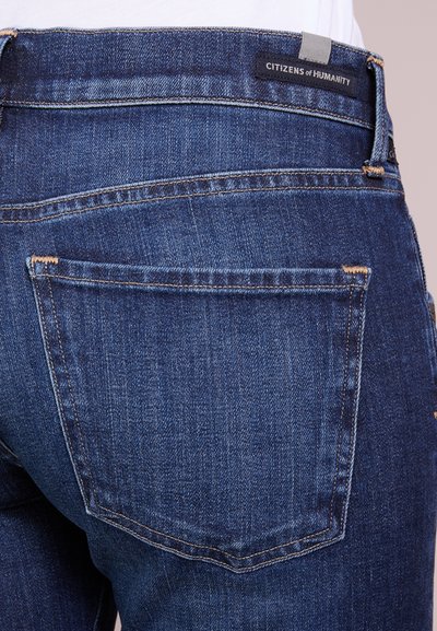 Donkerblauwe denim jeans met een rechte pasvorm, zichtbaar stiksel en twee achterzakken. Etiket leest "CITIZENS of HUMANITY."