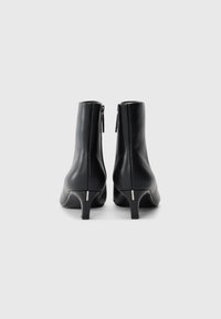 Pair of black ankle boots with kitten heels and back zippers on a plain white background.