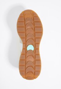 Suola della scarpa caratterizzata da un motivo testurizzato in gomma beige, con accenti arrotondati e un logo circolare blu centrale.