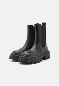 Botas de tobillo de cuero negro con paneles laterales elásticos, suelas de plataforma gruesas y suelas externas de goma texturizada. Acabado liso con un detalle mínimo.