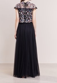 Jupe longue en tulle noir avec un corsage à manches courtes brodé de fleurs. Comprend une fermeture nouée au niveau du cou et des manches transparentes volantées.