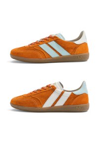 Deux baskets en daim orange avec semelles en gomme, l'une affichant des rayures bleu clair, l'autre des rayures blanches, toutes deux avec des lacets et des détails de marque.