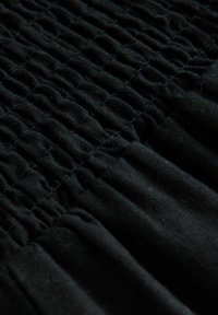 Tissu noir avec une texture froncée, comportant des plis horizontaux cousus dans un motif cohérent. Matériau doux avec une finition lisse.