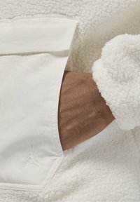 Hvid fleecejakke med en struktureret, fluffy overflade. Har et broderet Jordan-logo i hvid. Viser en tætsiddende, elastisk manchette.
