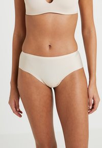 Ensemble de sous-vêtements beige présentant un design sans coutures. Le tissu est lisse avec une finition mate, et la coupe offre une couverture complète.