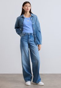 Τζιν μπουφάν πάνω από ανοιχτό γαλάζιο ριπ τοπ, σε συνδυασμό με τζιν παντελόνι ψηλόμεσο με φαρδιά πόδια. Το σύνολο ολοκληρώνουν λευκά αθλητικά παπούτσια.