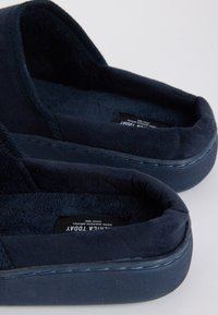 Chaussons bleu marine avec une tige douce et texturée et une semelle intérieure rembourrée. Forme arrondie avec des coutures autour du bord.