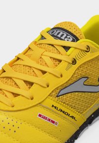 Φωτεινό κίτρινο αθλητικό παπούτσι με επάνω μέρος από δίχτυ, κίτρινα κορδόνια, γκρι λογότυπο και το κείμενο "Mundial" στο πλάι, σχεδιασμένο για εξωτερική χρήση.