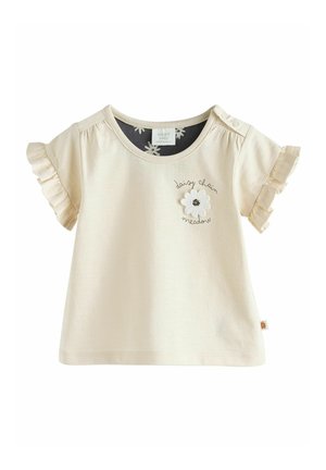 Camiseta de manga corta en crema clara con mangas con volantes, detalle de flores bordadas y texto "pradera de cadenas de margaritas". Material de algodón.