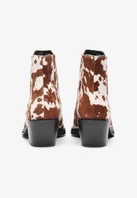 Καφέ και λευκές γούνινες γυναικείες μπότες ankle με λεία υφή, στρογγυλεμένη μύτη και χαμηλό τακούνι τύπου block. Η πίσω όψη αποτυπώνει χαρακτηριστικό μοτίβο γούνας.
