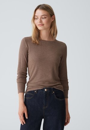 Braun geripptes Langarmshirt mit Rundhalsausschnitt, kombiniert mit dunkelblauen Jeans. Der Stoff wirkt weich und hat eine figurbetonte Silhouette.