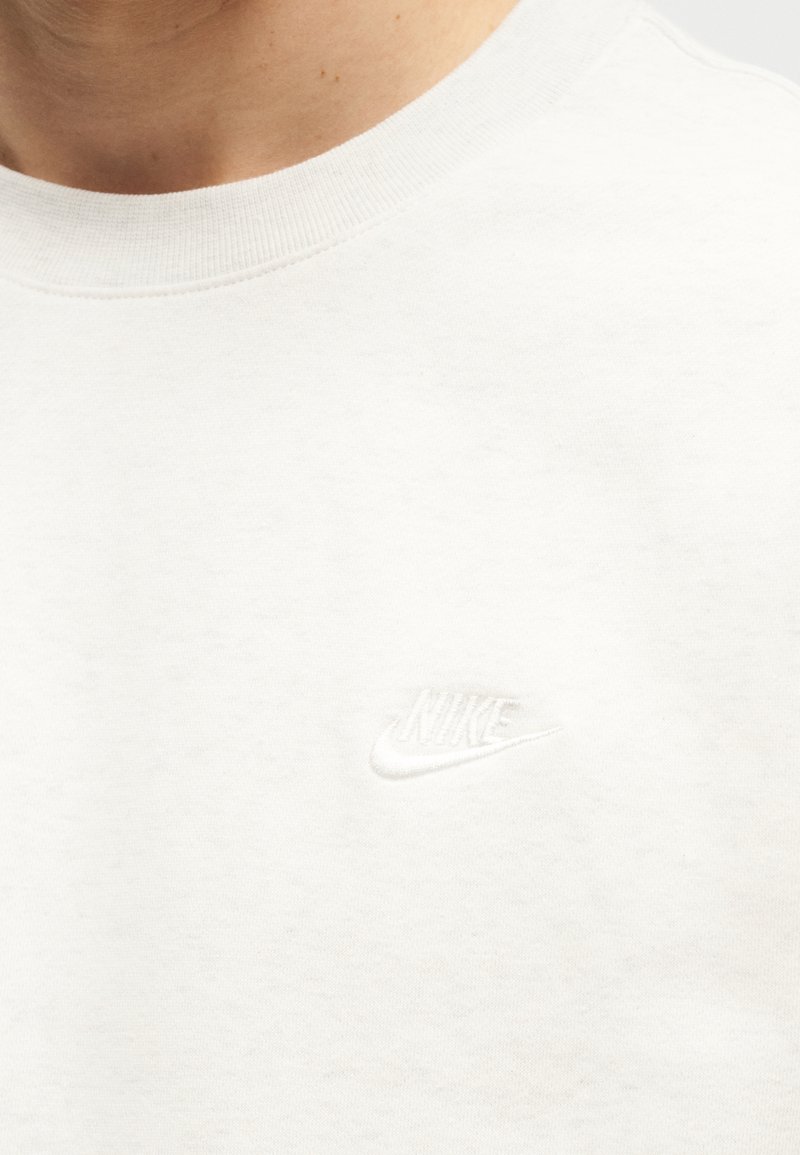 Primo piano di una persona che indossa una t-shirt girocollo bianca semplice di Nike con un piccolo logo Nike ricamato sul petto.