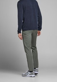 Tenue décontractée composée d'une chemise à manches longues bleu foncé, d'un pantalon vert olive et de baskets grises avec des accents blancs, vue de dos.