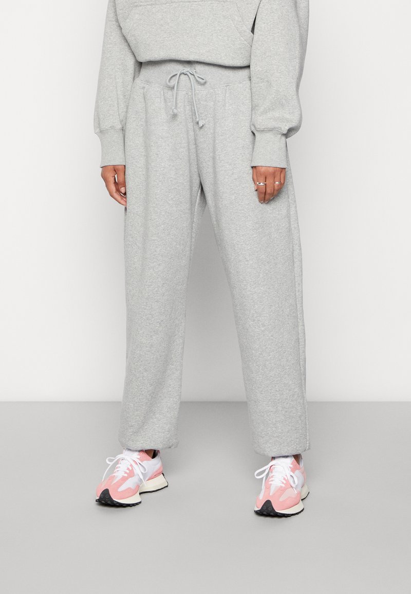 Hellgraue, hochtaillierte Sweatpants mit elastischem Bund und Kordelzug, aus weichem Stoff gefertigt. Kombiniert mit rosa-weißen Turnschuhen.
