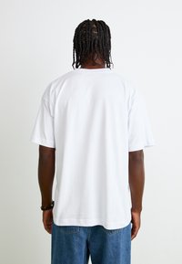 Hvid bomulds T-shirt med korte ærmer, lige pasform og rund halsudskæring; båret med blå denim jeans, der har et sømløst bagview.