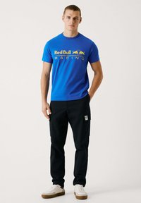 Kuning sinine t-särk, millel on kollane "Red Bull Racing" tekst, kombinatsioonis mustade cargo-pükste ja valgete sneakeritega, millel on beež aktsent.