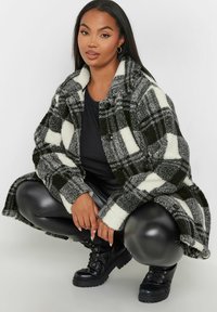 Svart och vit rutigt fleecejacka med krage, knappstängning och långa ärmar; bärs över en svart topp och kombineras med läderbyxor och stövlar.