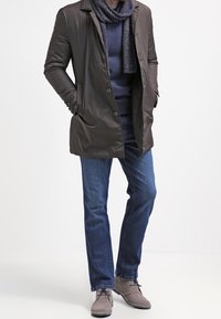 Tmavě hnědý zateplený kabát s límečkem, zapínáním na knoflíky a dvěma bočními kapsami, doplněný tmavými džínami a světle šedými kotn�íkovými botami.