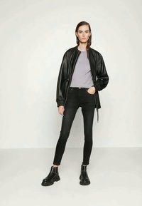 Mustat nahkabomberitakki vaaleanharmaan paidan päällä, yhdistettynä mustiin kapeisiin farkkuihin ja mustiin nilkkasaappaisiin. Tasainen pinta ja istuva tyyli.