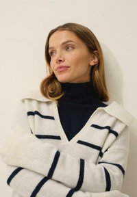 Gräddstrimmig tröja med V-ringning och bred krage, med marinblå ränder och ribbade ärmslut, kombinerad med en svart polotröja.