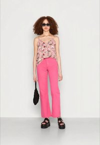 Camisola floral rosa com detalhes verdes, emparelhada com calças rosa de cintura alta e boca de sino. A modelo usa óculos de sol pretos e uma bolsa preta texturizada.