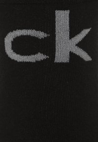 Juodas kojinės su ryškiu pilku "ck" logotipu. Medžiaga atrodo lygi, su minkšta, tampria tekstūra ir giliu akcentu viršuje.