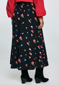 En person i en r�ød sweater står med ryggen til betrakteren, iført en sort blomsterkjole og sorte hæl støvler.