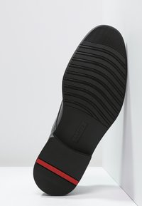 Black rubber shoe sole with textured grooves and a red accent stripe. Features a curved shape and slight arch for support.