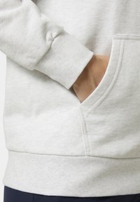 Sudadera gris claro que muestra una tela suave y texturizada. Las características incluyen un bolsillo en el costado y puños de canalé.
