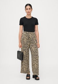 Zwart kortmouwtop met zilveren studs, gecombineerd met beige panterprint wijde broek, zwarte tas en zwarte plateau sandalen.