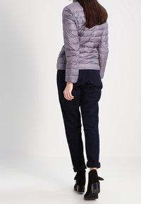 Jasnoszara kurtka puchowa o dopasowanym kroju, poziomym pikowaniu i wysokim kołnierzu. W zestawieniu z ciemnoniebieskimi spodniami z mankietami i botkami za kostkę.