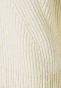 Gros plan sur un tissu tricoté de couleur crème avec des lignes verticales côtelées et un motif texturé diagonal.