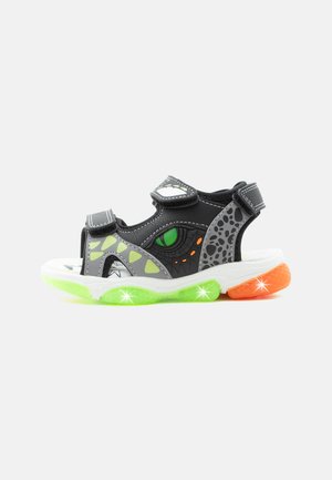 Children’s black and gray sandal with green and orange glowing sole lights and an eye and scale design on the side.