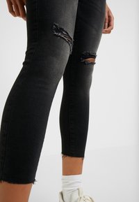 Svarta denimjeans med en tight design, med revor vid knäna, fransade fållar och en slät yta. Utsmyckade med synliga sömmar.