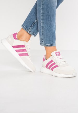 Sneakers z beżową cholewką z zamszu i tkaniny, z różowymi paskami, białymi sznurówkami i teksturowaną białą podeszwą.