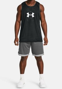 Camiseta de tirantes negra de malla con un gran logo blanco, combinada con pantalones cortos grises que tienen franjas blancas en los lados. Calzado deportivo completa el conjunto.