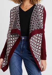 Burgundy öppen front cardigan med en mönstrad grå-vit bakpanel, med långa ärmar och en avslappnad passform. Texturerat stickat tyg.