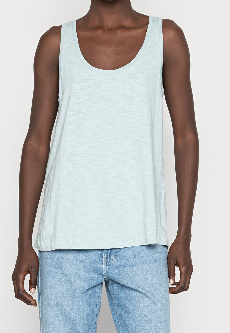 Lichtblauw tanktop met een ronde hals en mouwloos ontwerp. Gemaakt van een gestructureerde stof met een relaxte pasvorm. Draagt met lichtblauwe jeans.