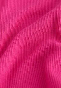 Kirkkaan pinkki ribbineulos, jossa pehmeät laskokset luovat tekstuurisen, aaltoilevan pinnan.