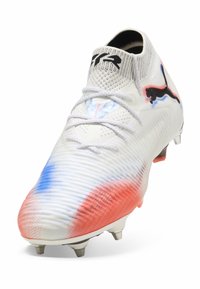 Weißer Fußballschuh mit strukturiertem Obermaterial, blauen und roten Farbverlauf- Akzenten, schwarzem Logo, Schnürverschluss und konischen Stollen an der Sohle.