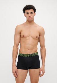 Schwarze Boxershorts mit einem leuchtend gelben "UNDER ARMOUR"-Bund. Der Stoff wirkt glatt und hat ein eng anliegendes Design.